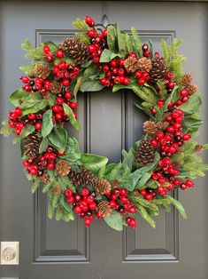 a christmas wreath with pine cones, holly and red berries on the front door frame