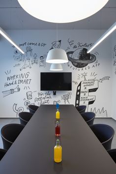 an empty conference room with black chairs and chalk drawings on the wall behind it, along with a bottle of orange juice