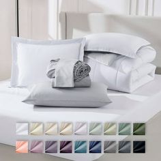 a bed with white sheets, pillows and blankets on top of it in different colors