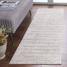 a white rug on top of a wooden floor next to a couch and potted plant