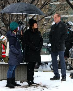 three people standing under an umbrella in the snow with other people behind them looking on