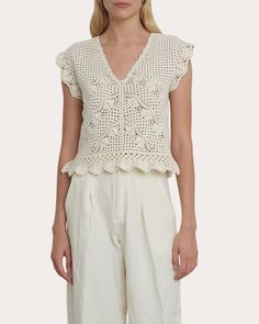 a woman is wearing white pants and a crochet top with ruffles