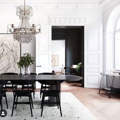 an elegant dining room with chandelier and black table in front of white paneled walls