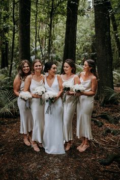 the bride and her bridesmaids pose for a photo in the woods with their bouquets