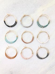 six pairs of hoop earrings with different colors and sizes on a white marble counter top