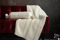 a red velvet couch with a white crocheted blanket on it and a black wooden floor