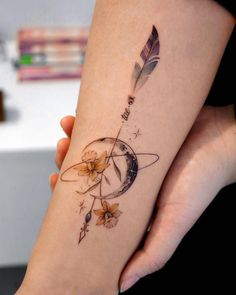 a woman's arm with a tattoo on it that has flowers and an arrow