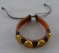 Brown Leather cuff bracelet adorned with gold Crux Sancti Patris encrusted coins. Bracelet is adjustable in size and one size fits all. Adjustable Gold Leather Cuff Bracelet, Handmade Gold Leather Bracelet, Adjustable Gold Leather Bracelet, Handmade Gold Leather Bracelet For Festivals, Handmade Gold Leather Bangle Bracelet, Gold Beaded Cuff Bracelets, Gold Bohemian Leather Bracelet Gift, Gold Cuff Beaded Bracelets For Gift, Gold Cuff Beaded Bracelet As Gift