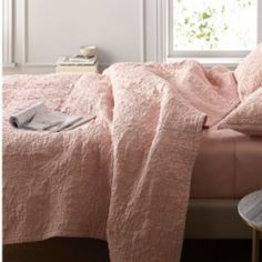 a bed with a pink comforter and pillows on top of it next to a window