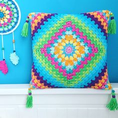 a colorful crocheted pillow sitting on top of a white shelf next to a blue wall