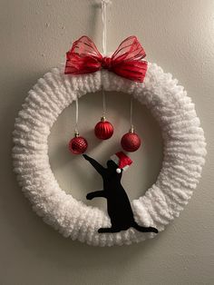 a black cat hanging from a white wreath with red ornaments on it's side