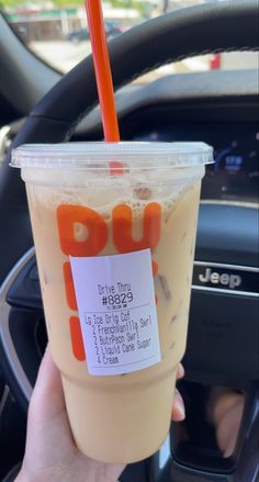 a person is holding up a drink in their hand and steering wheel behind the car