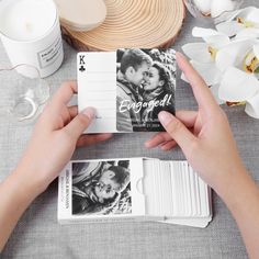 two hands holding cards next to each other on a table with flowers and candles in the background