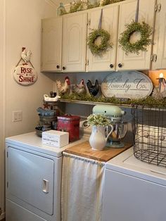 a white washer sitting in a kitchen next to a dryer and cabinets with wreaths on them