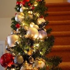 a christmas tree with ornaments and lights on it in front of some stairs, next to a stair case