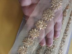 a woman's hand with gold beading on it and sheer curtains behind her