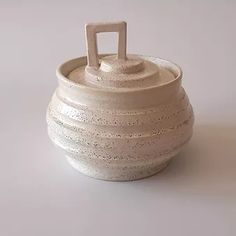 a white ceramic container with a handle on the top is sitting on a gray surface