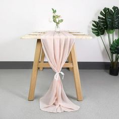 a table with a pink cloth draped over it and a plant in the corner next to it