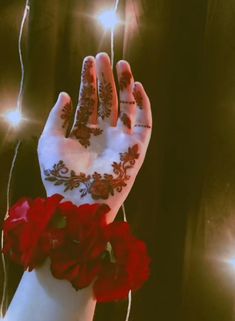 a person's hand with hendi and flowers on it, surrounded by string lights