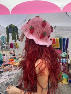 a woman with long red hair wearing a pink crochet strawberry hat on top of her head