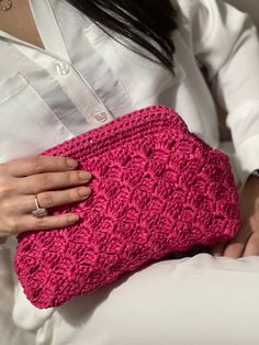 a woman is holding a pink crocheted purse in her hands and wearing a white shirt