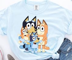 Celebrate family moments in style with our Bluey and Family T-shirt, a uniquely garment-dyed piece that carries the vibrant spirit of your favorite playful characters! This unisex tee features an adorable design showcasing Bluey, Bingo, Dad, and Mom, making it the perfect choice for fans looking to express their love for this beloved family. Crafted for comfort and durability, it's not just a shirt, but a canvas for joyful memories and imaginative play. Ideal for family outings, birthday parties Blue Family Matching Short Sleeve Tops, Light Blue Graphic Tee With Cartoon Print, Blue T-shirt With Character Print In Relaxed Fit, Light Blue Crew Neck T-shirt With Character Print, Blue Family Matching T-shirt With Character Print, Cute Soft-washed Blue Tops, Funny Blue T-shirt With Cartoon Print, Blue Cartoon Print Tops Relaxed Fit, Blue Cartoon Print Relaxed Fit Tops