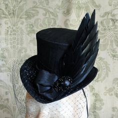 Simple yet full of impact,The Nevermore,this gothic mini top hat is utterly suitable for the darkest of appearances. Covered with black silk shantung, it is gracefully embraced with matching black band around the crown.It is elegantly embellished with a black feather, faux raven wing, Gothic Top Hat With High Crown, Steampunk Top Hat With Curved Brim For Costume, Gothic Fitted Hats With Curved Brim, Gothic Fitted Hat With Curved Brim, Gothic Fitted Hat With Short Brim, Gothic Fitted Top Hat With High Crown, Gothic High Crown Top Hat, Gothic Fitted Brimmed Top Hat, Fitted Gothic Hat With Curved Brim