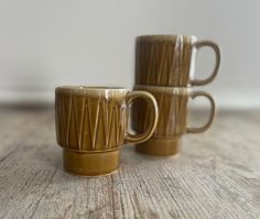 two brown coffee mugs sitting on top of a wooden table next to each other