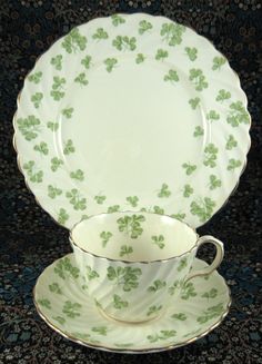 a cup and saucer with four leaf clover designs on them, sitting next to each other