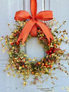 an orange bow hangs on the front door of a white door with a wreath and berries