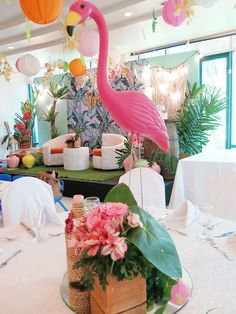 a pink flamingo sitting on top of a table next to a basket filled with flowers