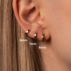 a woman's ear is shown with two small gold hoop earrings