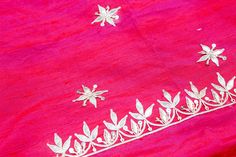 an embroidered piece with flowers and leaves on the side, sitting on top of a pink cloth