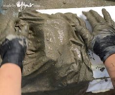 two hands are covered in mud while another person is working on the ground with gloves