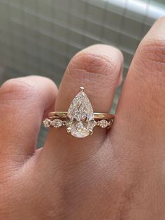 a person's hand holding a ring with a pear shaped diamond in it and three smaller diamonds on the band