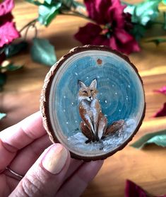 a hand holding up a small piece of wood with a painting of a fox on it