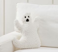 a white teddy bear sitting on top of a couch next to a pillow with its arms in the air