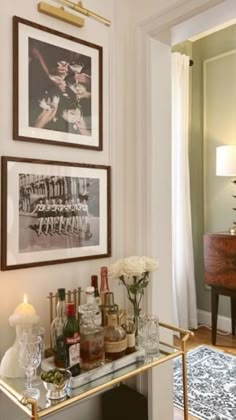 a bar cart with liquor bottles on it in front of two framed pictures and a chandelier