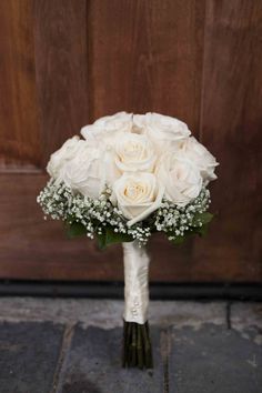 a bouquet of white roses and baby's breath sits in front of a wooden door