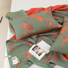 a bed with green and orange bedspread on top of it next to a book