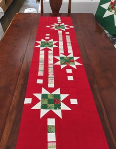 a red table runner with green and white quilted stars on it, sitting on a wooden dining room table