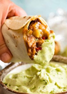 a burrito being dipped with guacamole in a bowl