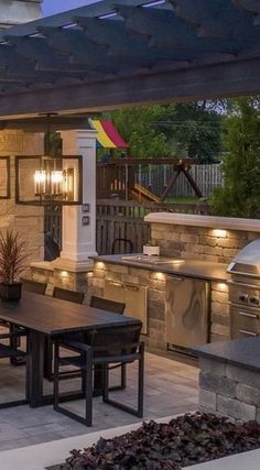 an outdoor kitchen and dining area is lit up at night with lights on the grill