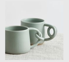 two green mugs sitting next to each other on top of a white table cloth