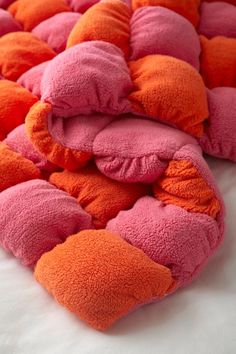 a pile of pink and orange pillows sitting on top of a white bed covered in blankets