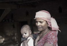 a woman holding a baby in her arms and wearing a pink head scarf on top of her head