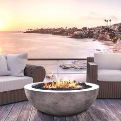 an outdoor fire pit sitting on top of a wooden deck next to the ocean at sunset