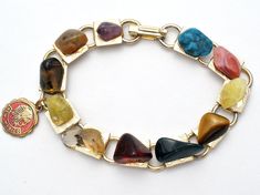 Multi Color Jewelry - This is a gold tone link bracelet with nugget gems of turquoise, amethyst, jasper, agate, tiger's eye, rhodocrosite and more. It has a round red enamel New Mexico charm that measures .5" in diameter, bracelet is 7" long and .38" wide. Vintage Gold Bracelets With Natural Stones, Multicolor Metal Bracelets With Stones, Vintage Multicolor Stone Bracelets, Multicolor Costume Jewelry Bracelets With Jewels, Vintage Multicolor Agate Jewelry, Multicolor Jewel Costume Jewelry Bracelets, Vintage Multicolor Natural Gemstones, Multicolor Jewelry, Color Jewelry