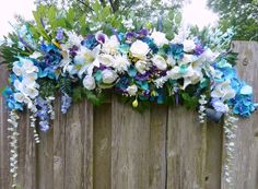 an arrangement of blue and white flowers on a wooden fence