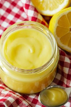 a jar filled with lemon curd next to sliced oranges on a checkered table cloth